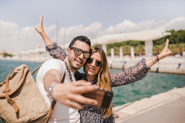 Foto gratuita uomo sorridente che prende selfie sul telefono cellulare con la sua gesturing della fidanzata