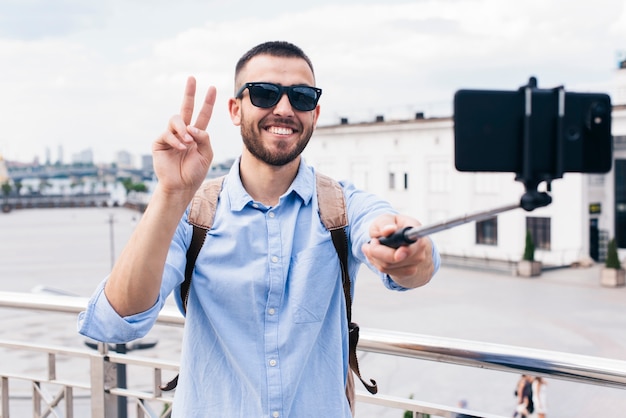 携帯電話で勝利のジェスチャーでselfieを取って笑みを浮かべて男