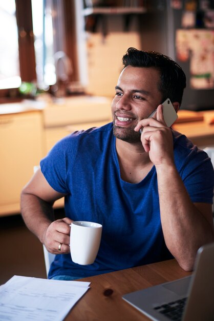 Smiling man talking by mobile phone and drinking coffee