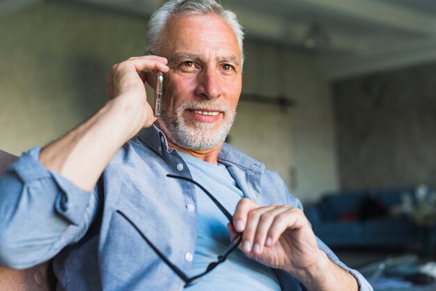 Smiling man talking on mobile phone holding black eyeglasses