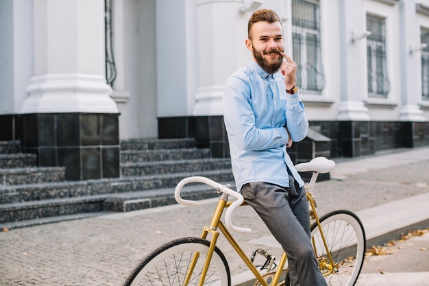 Smiling man touching moustache near bicycle