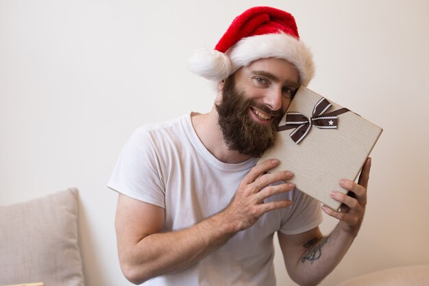 Улыбающийся человек пытается угадать, что находится внутри рождественской подарочной коробке