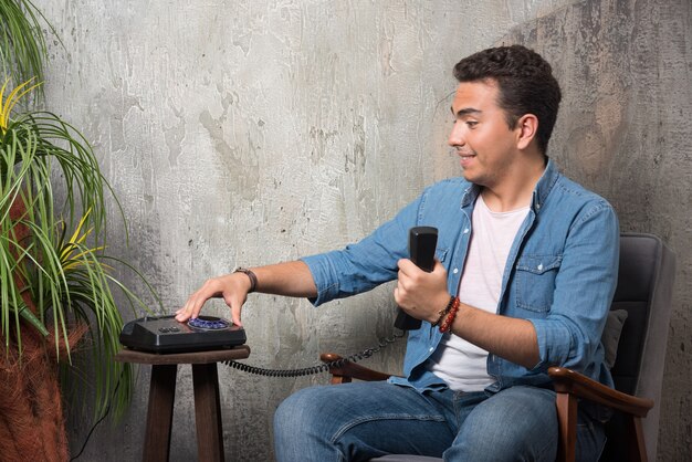 Smiling man typing a number on telephone and sitting on chair. High quality photo