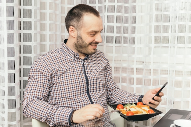 Foto gratuita uomo sorridente che utilizza smartphone durante la cena