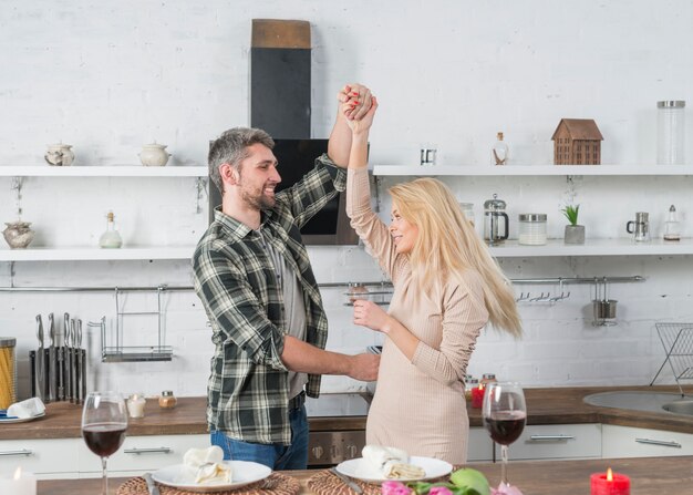 Smiling man whirling woman near table in kitchen