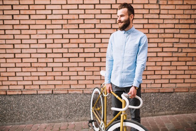 Smiling man with bicycle near brick wall