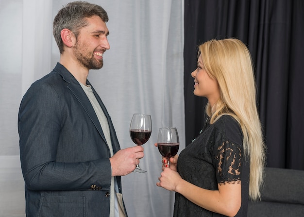 陽気な女性の近くのワインのグラスを持つ男の笑みを浮かべてください。