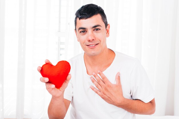 Улыбающийся человек с рукой на груди держит декоративное сердце