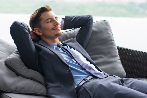 Smiling man with hands behind head dozing on couch