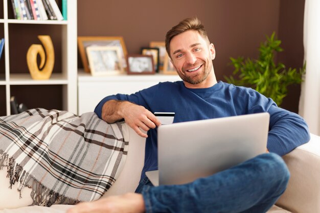 Smiling man with laptop and credit card on sofa