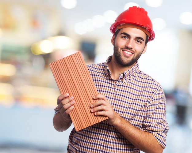 Uomo sorridente con casco rosso e un mattone