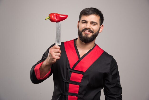 Smiling man with red pepper on knife.