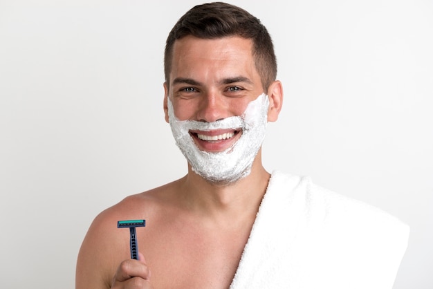 カメラ目線かみそりを保持しているシェービングクリームを適用したタオルで笑みを浮かべて男