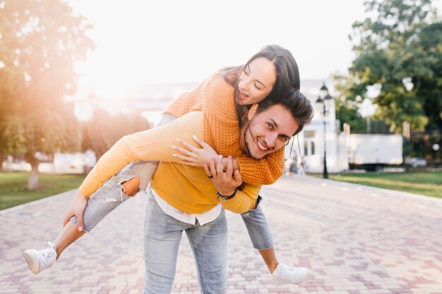 晴れた秋の日に友人のピギーバックを運ぶトレンディな髪型の笑顔の男