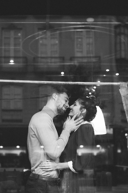 Smiling man and woman hugging in restaurant near window 