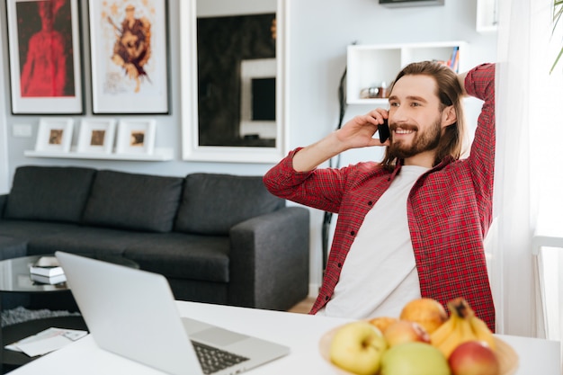 Uomo sorridente che lavora con il computer portatile e che parla sul telefono cellulare