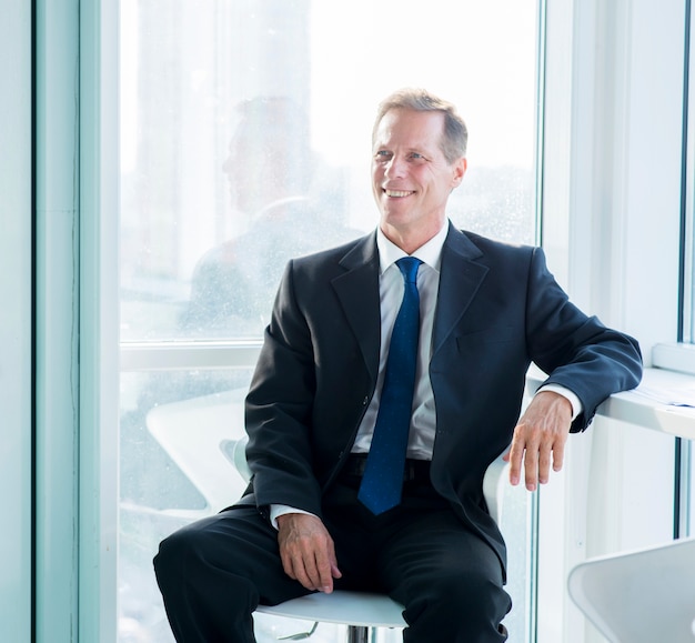 Smiling mature businessman sitting on stool in office