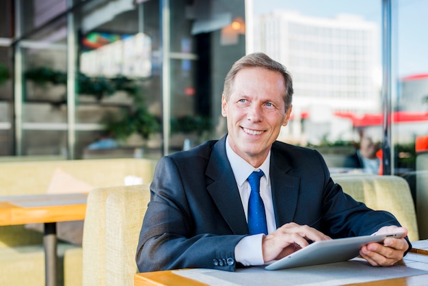 Smiling mature businessman using digital tablet in caf�