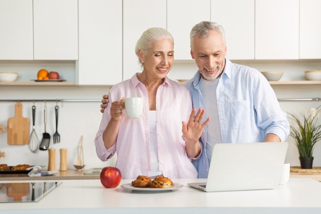 Smiling mature loving couple family eating pastries while using laptop