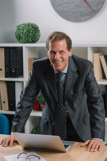 Smiling mature male lawyer with laptop on wooden table in the courtroom