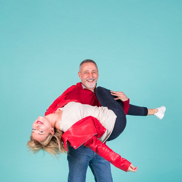 Smiling mature man carrying his wife against turquoise background