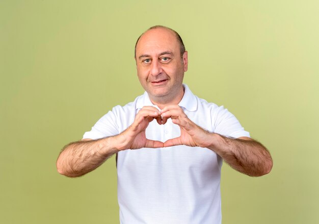 Улыбающийся зрелый мужчина показывает жест сердца, изолированный на оливково-зеленой стене