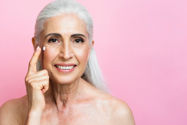 Smiling mature woman applying moisturizer