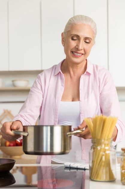 キッチン料理で立っている笑顔の成熟した女性