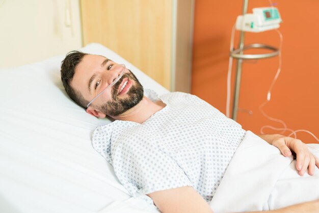 Улыбающийся взрослый пациент с кислородом лежит на больничной койке во время лечения
