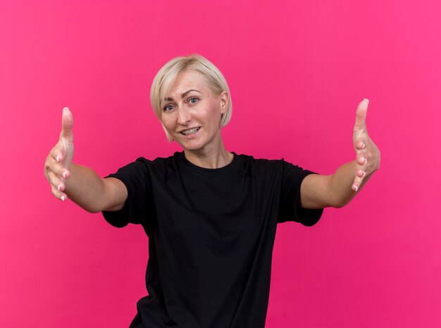 Smiling middle-aged blonde slavic woman doing size gesture looking at camera isolated on crimson background