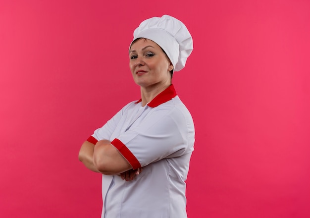 Smiling middle-aged female cook in chef uniform crossing hands with copy space
