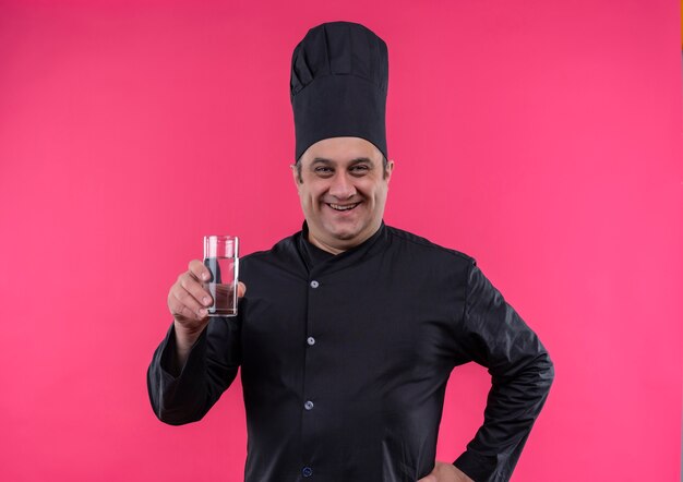 Smiling middle-aged male cook in chef uniform holding glasses of water