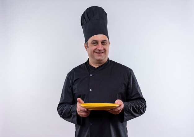 Smiling middle-aged male cook in chef uniform holding plate