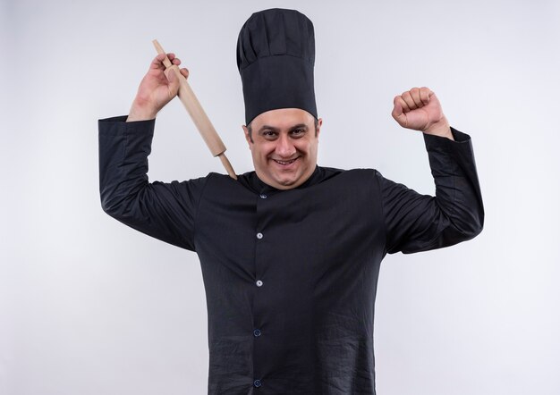 Foto gratuita cuoco maschio di mezza età sorridente in uniforme del cuoco unico che alza il mattarello che mostra forte gesto