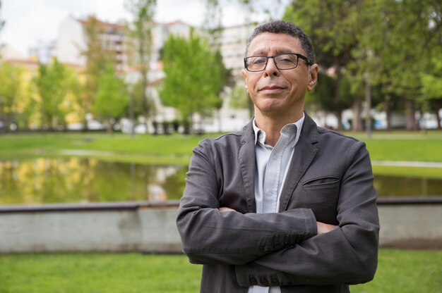 Smiling middle-aged man posing at camera and standing in park