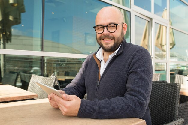 Smiling middle-aged man using tablet in street cafe