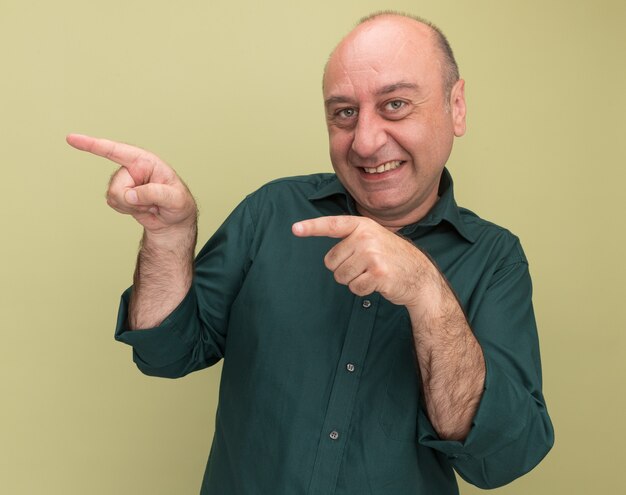 Smiling middle-aged man wearing green t-shirt points at side isolated on olive green wall