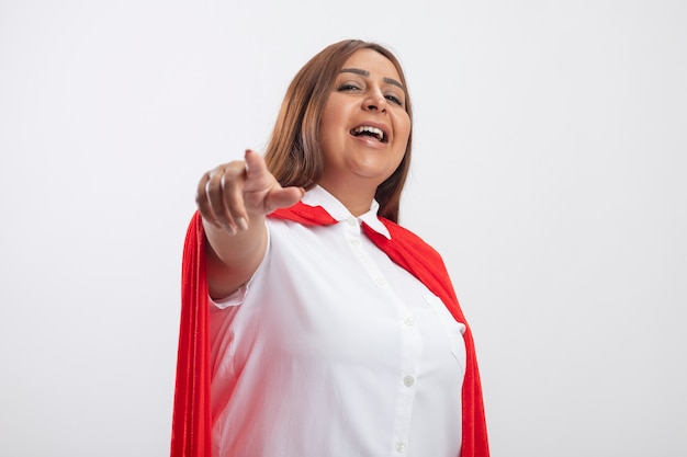 Smiling middle-aged superhero female looking at camera showing you gesture isolated on white