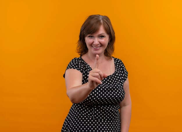 Улыбающаяся женщина средних лет, указывая пальцем на изолированную оранжевую стену с копией пространства