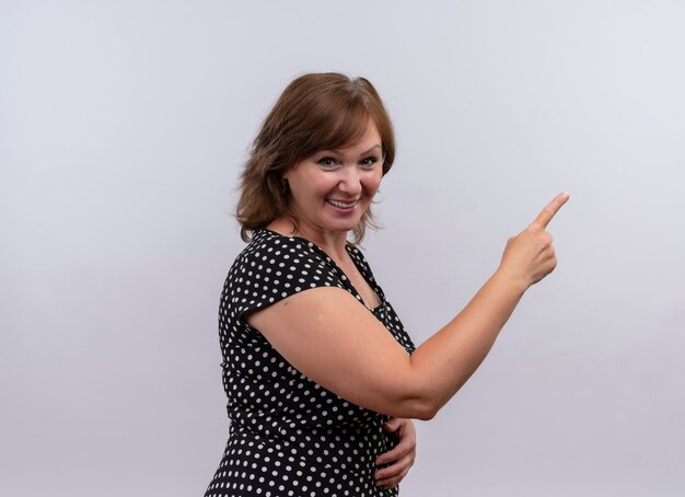 Улыбающаяся женщина средних лет, указывая пальцем на правую сторону на изолированной белой стене