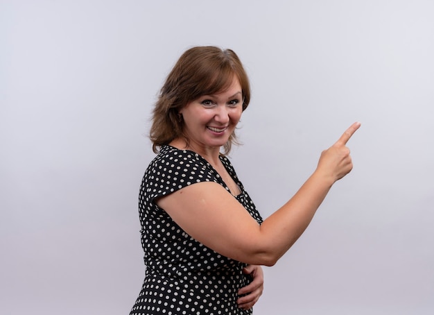 smiling middle-aged woman pointing with finger at right side on isolated white wall