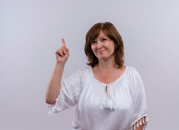 Smiling middle-aged woman pointing with finger up on isolated white wall