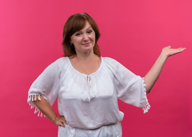 Foto gratuita donna di mezza età sorridente che mostra la mano vuota sulla parete rosa isolata