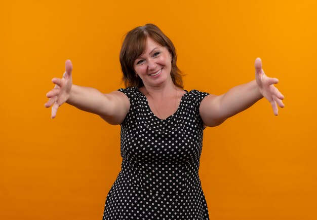 smiling middle-aged woman stretching hands on isolated orange wall