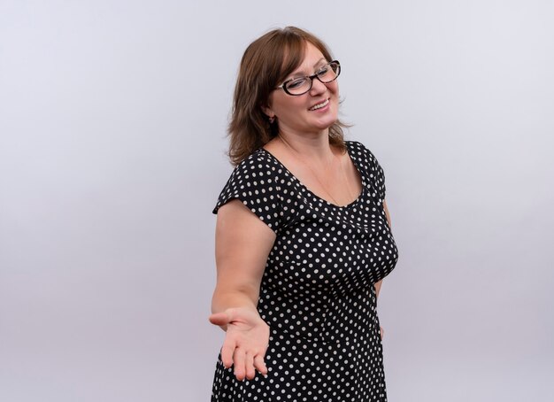 smiling middle-aged woman wearing glasses and showing empty hand on isolated white wall