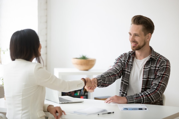 Smiling millennial partners handshaking in office thanking for successful teamwork