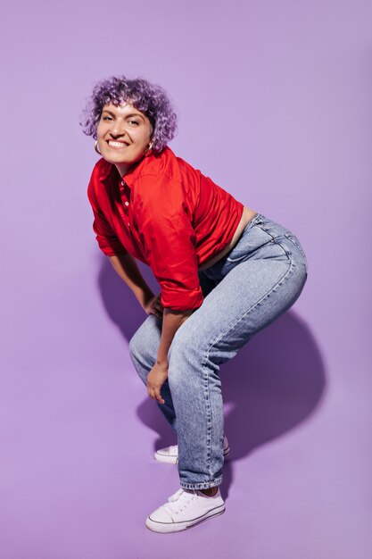 Smiling mischievous woman with curly hair in stylish bright clothes and white shoes posing