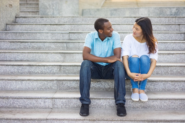 混乱したレースの男性と女性が階段で話すのに座って笑う。