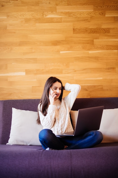 Smiling model working on a laptop sitting on the bed in the house