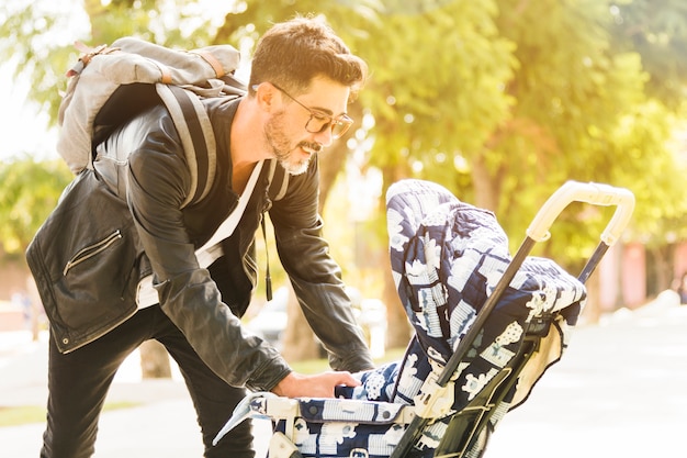 Free photo smiling modern man with his backpack taking care of his baby in the park